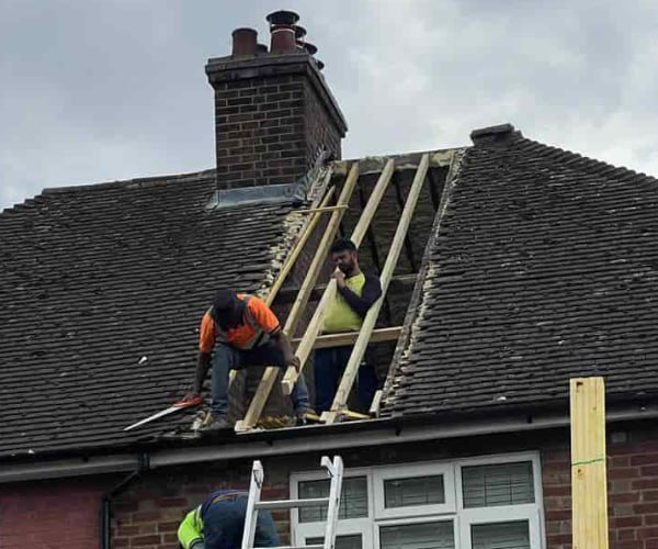 This is a photo of a roof repair being carried out. A section of the roof has been stripped and two roofers are replacing the rafters. Works being carried out by KAD Roofing Bircotes